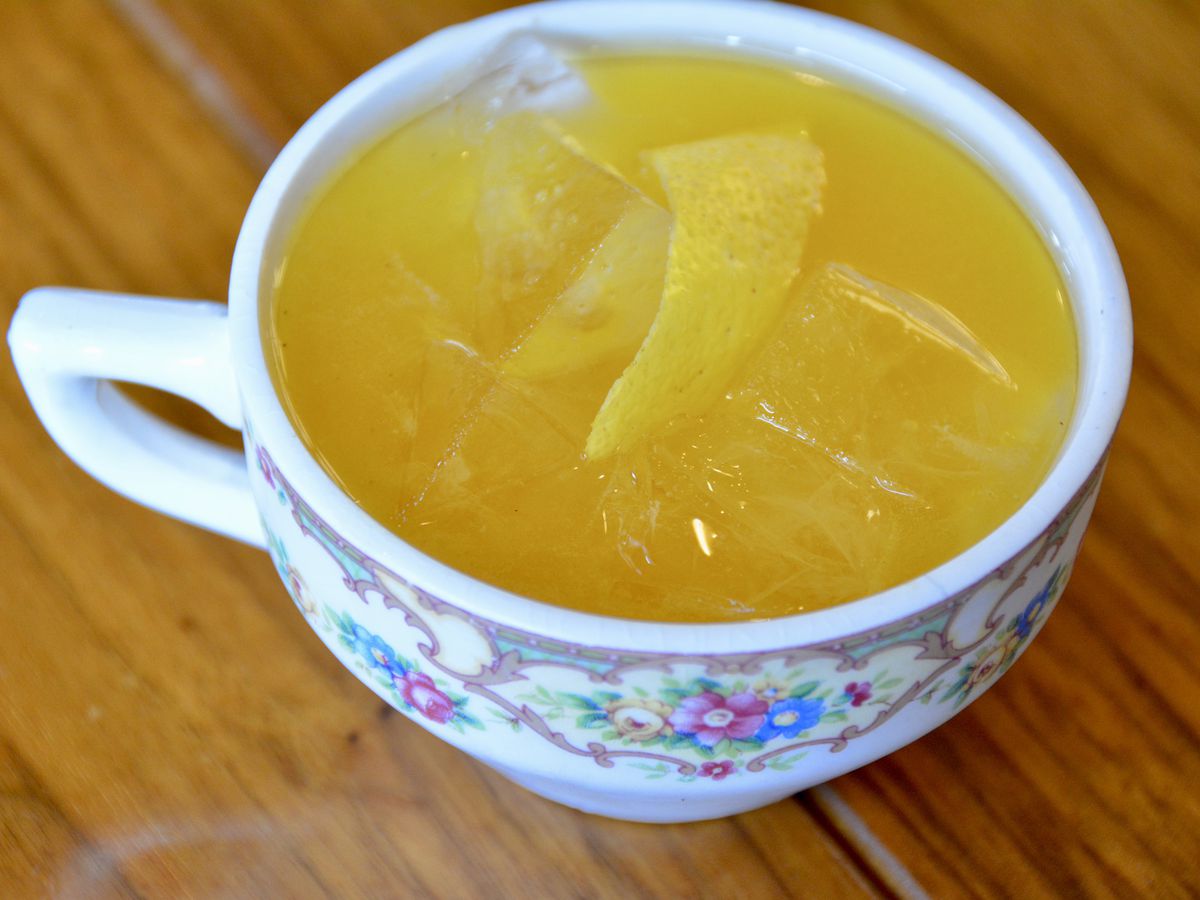 A short white tea cup holding a yellow-colored drink.