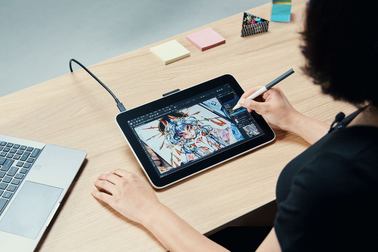 A lifestyle image of someone using a new Wacom One display tablet to illustrate a blue-haired cartoon character.