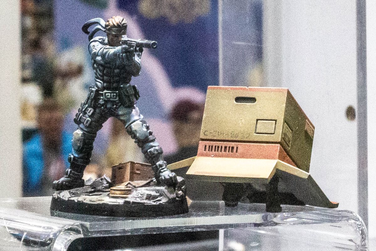 A photo shows Solid Snake, with and without a cardboard box, in painted miniatures from Gen Con 2023.