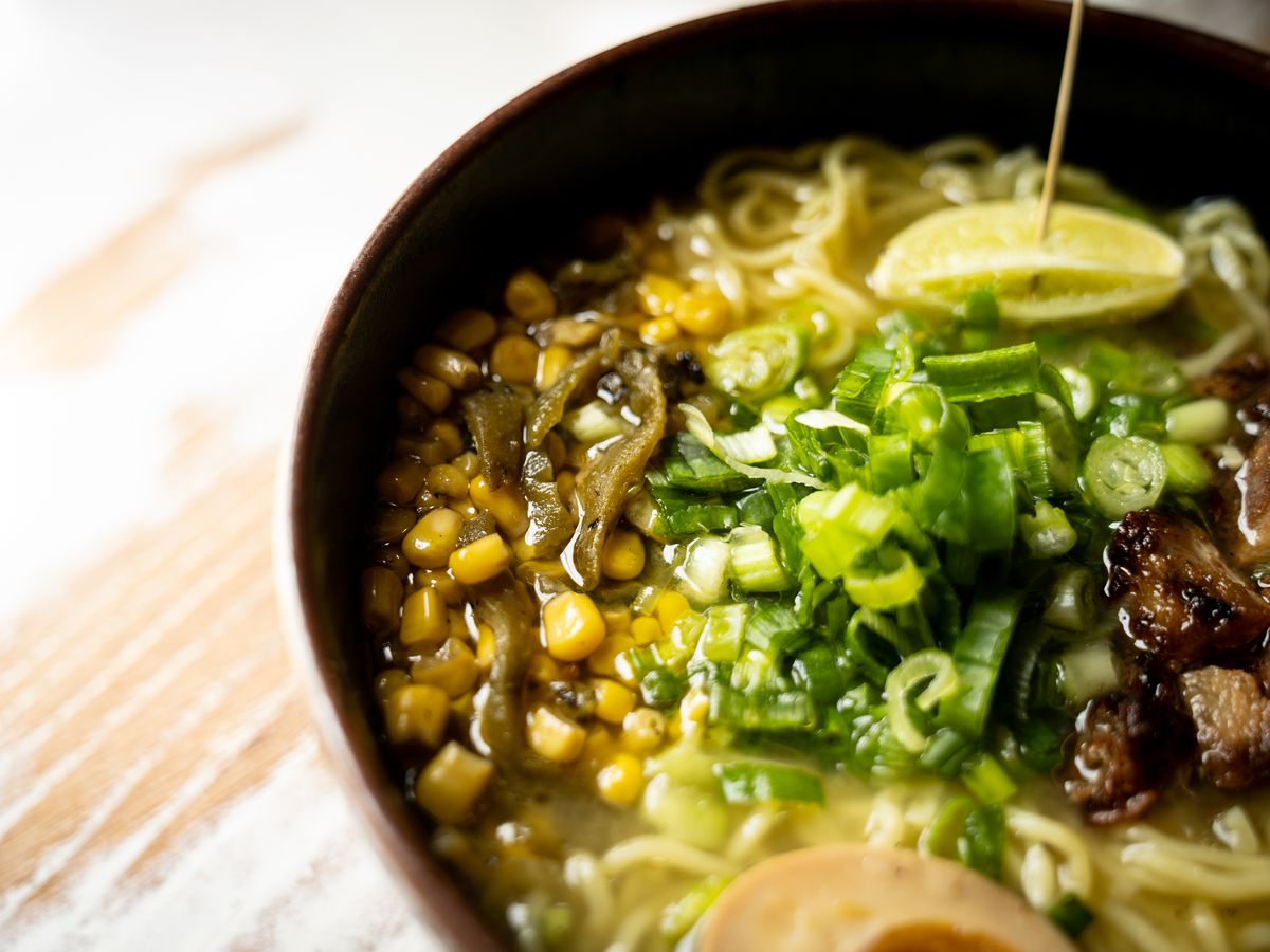 A bowl of ramen with noodles, broth, sliced green peppers.