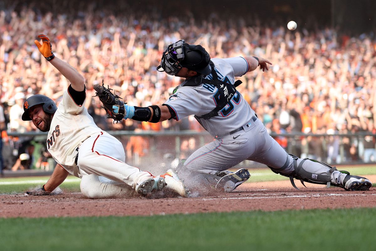 Darin Ruf #33 of the San Francisco Giants slides safely past Jacob Stallings #58 of the Miami Marlins to score the winning run on a hit by Austin Slater #13 in the tenth inning of their opening day game at Oracle Park
