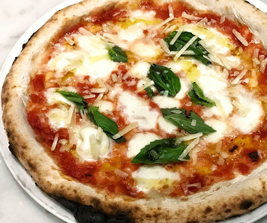 Closeup on a Margherita pizza with a slightly charred, wood-fired crust and a fresh basil topping.