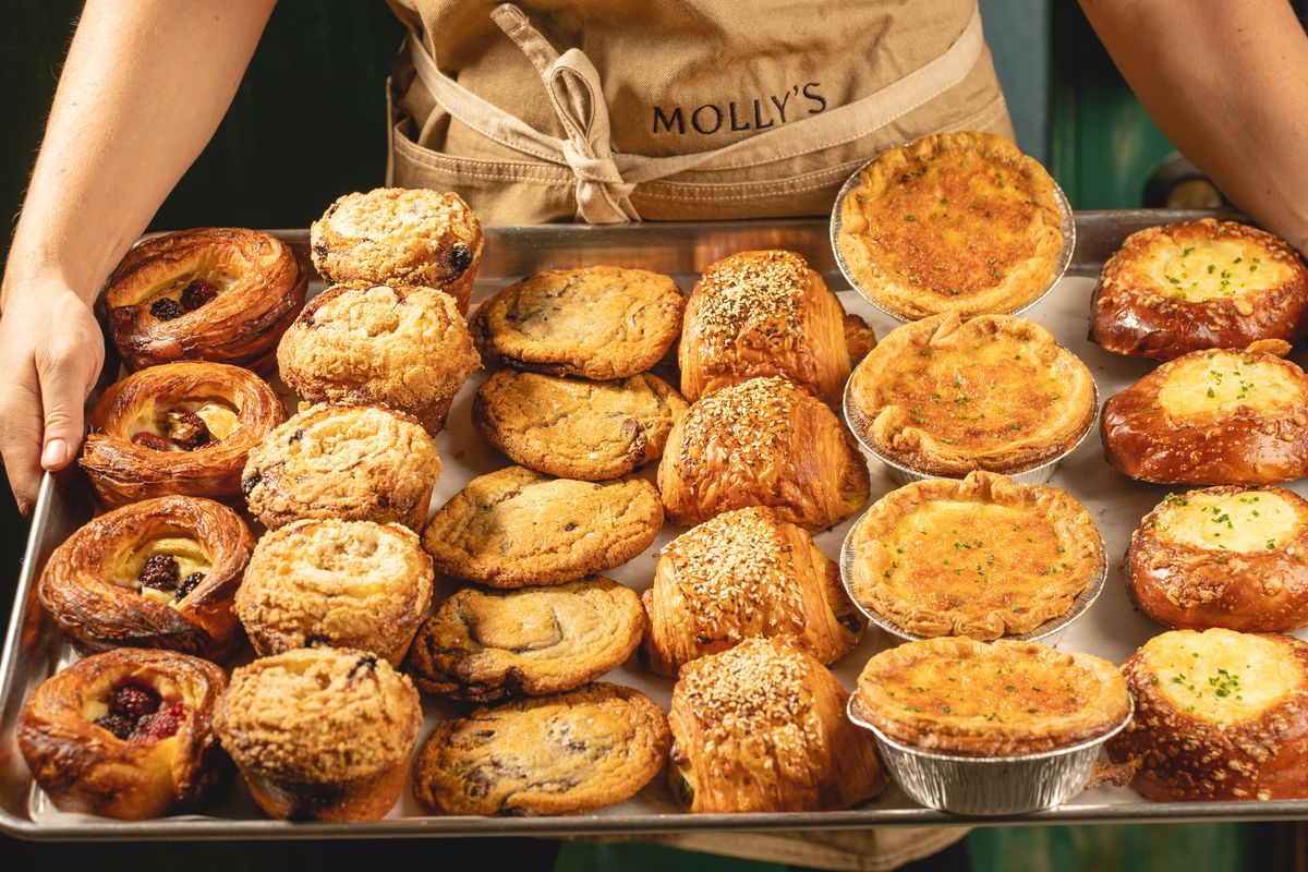 A person holds a tray of assorted pastries and cookies.
