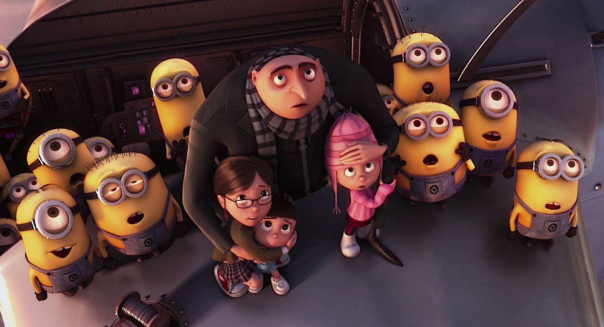 Animated anti-hero Gru shelters his three orphan adoptees in his arms while surrounded by Minions, as everyone in the image looks upward with their mouths hanging open in Despicable Me.