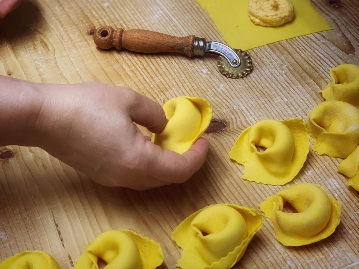 A person’s hand shapes tortelloni on a wood surface with a cutter nearby