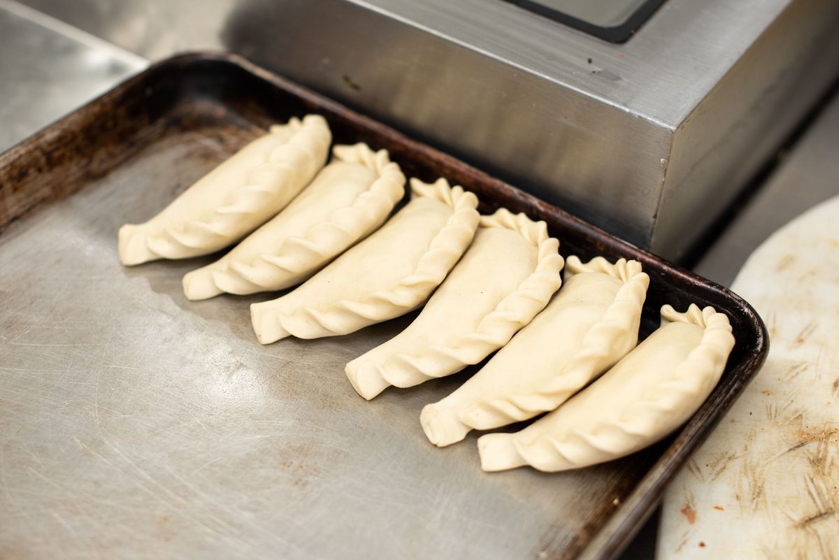 Lining up uncooked empanadas on a metal tray inside a restaurant.