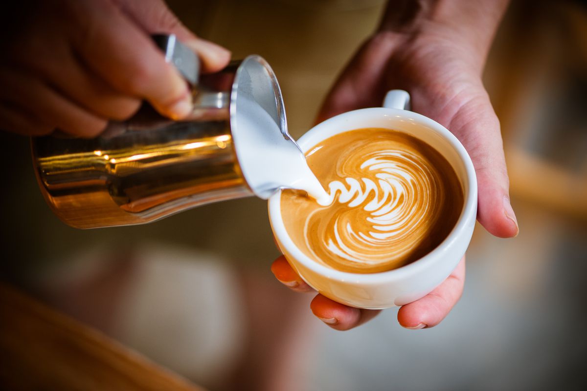 Milk is poured artfully into a coffee mug, making a foamy white pattern on top of the espresso.