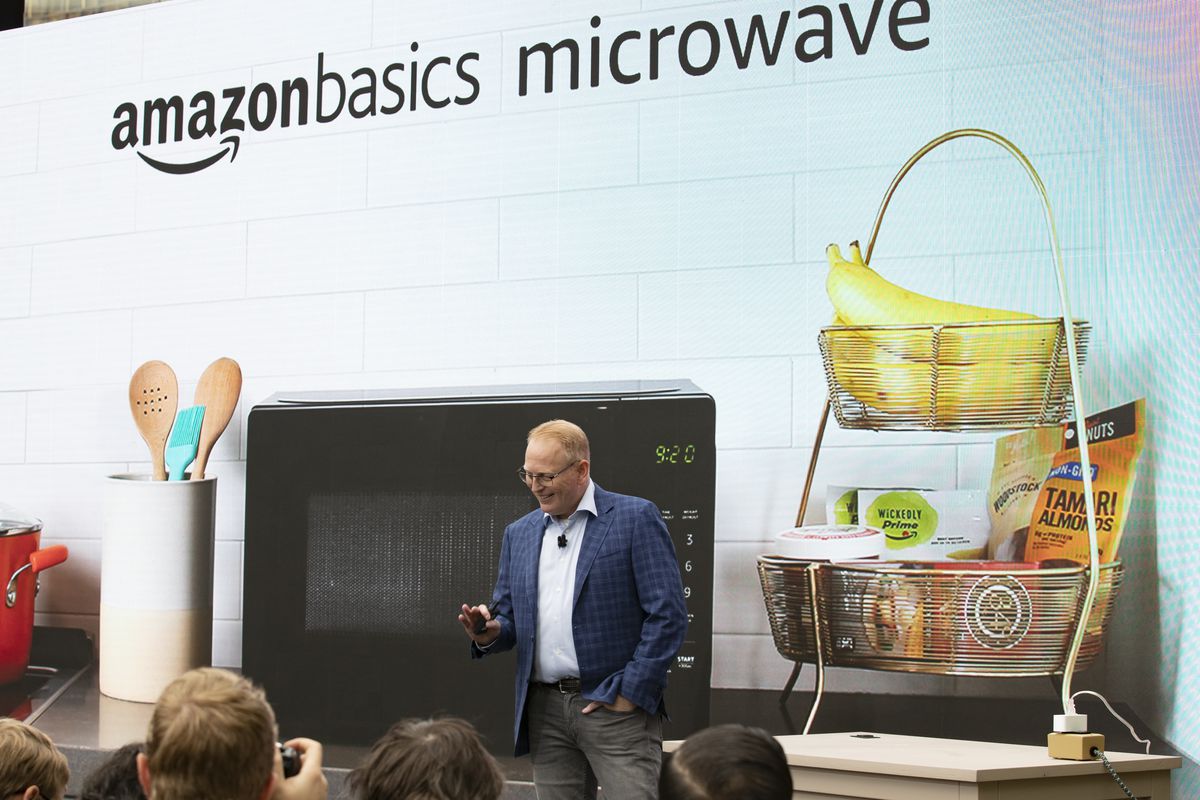 Senior VP of Amazon Devices Dave Limp in front of a picture of an Alexa-enabled microwave