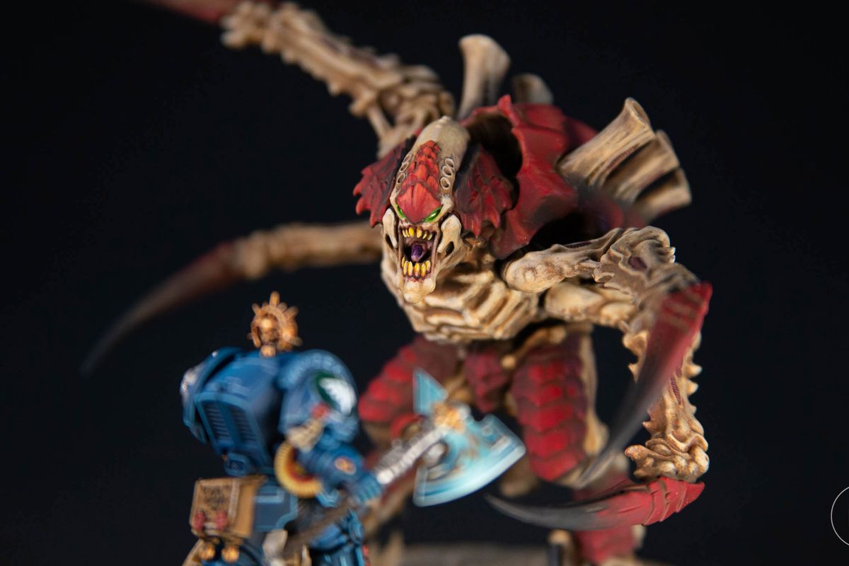 A close-up of a Screamer-Killer Tyrannid against a black background, closing in on a Terminator Librarian Space Marine. The image has a fairly short depth of field.