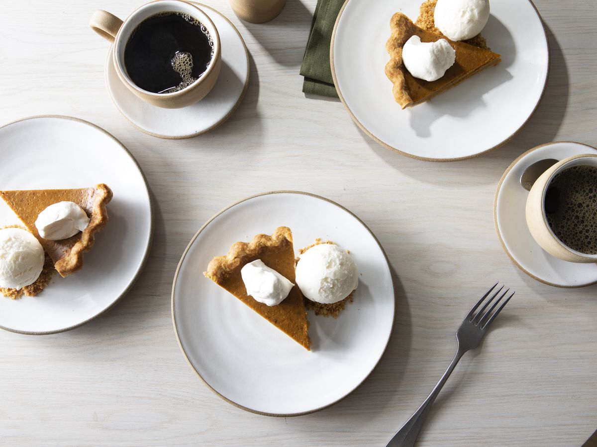 Slices of pumpkin pies on plates with cups of black coffee.