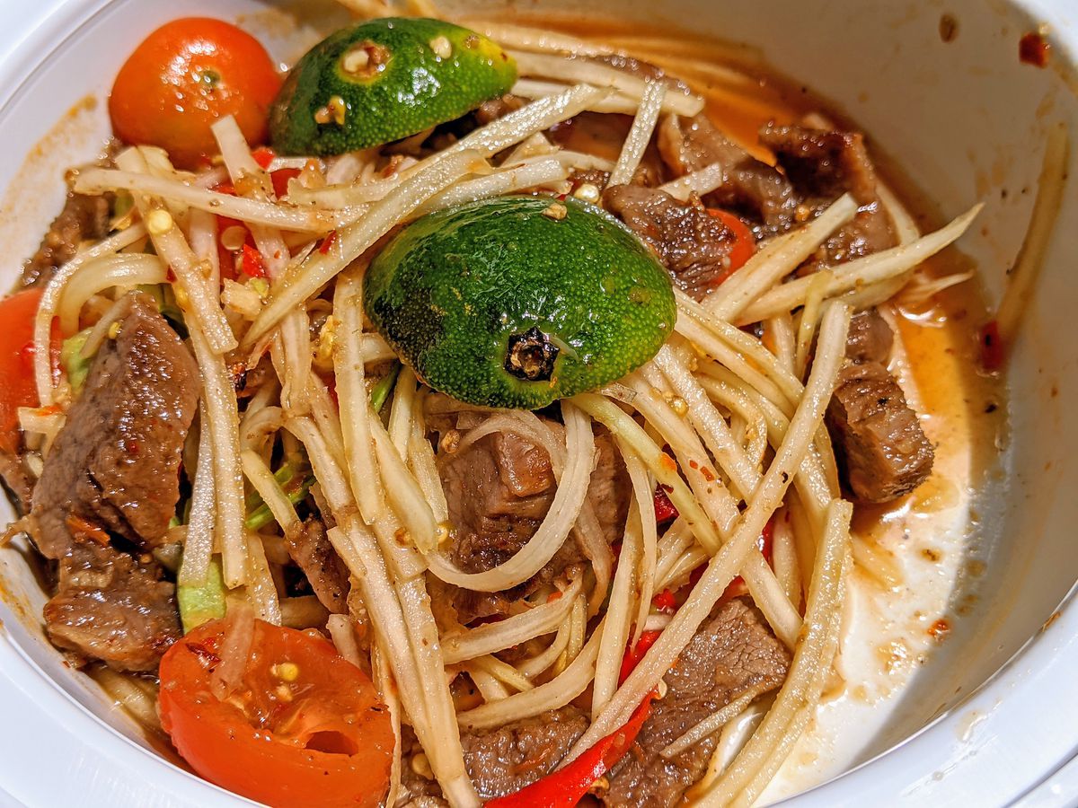 a close up of a white bowl with pieces of tomato, lime, beef, and green shoots