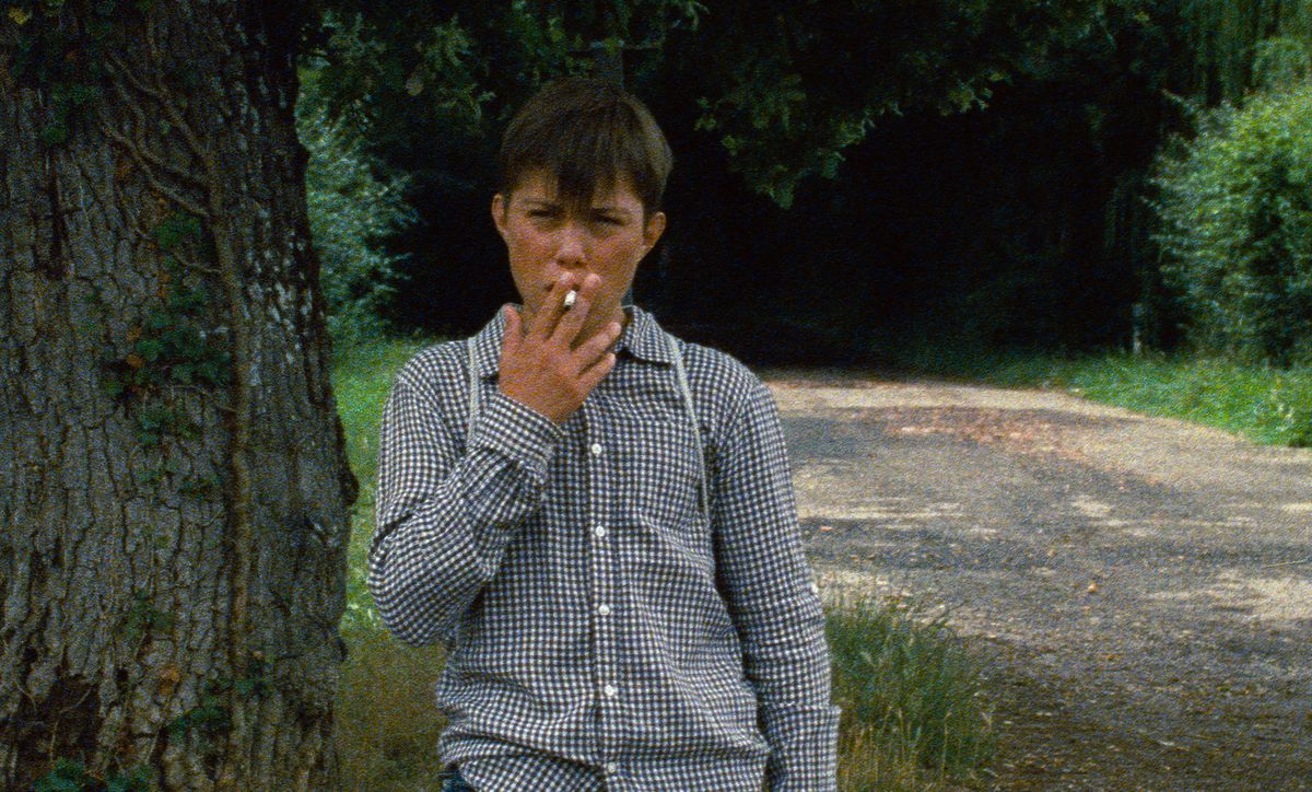 A very young boy smokes a cigarette in a grainy image from Astrakan