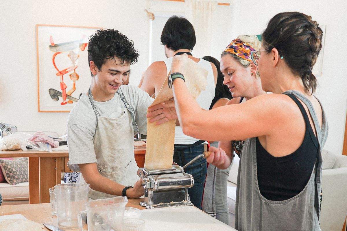 Three students gather around a pasta machine, making ramen dough.