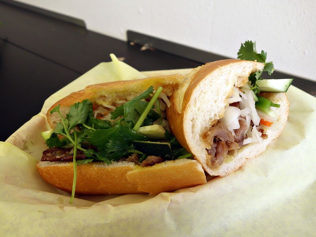 A banh mi sandwich filled with meat, cilantro, and sliced cucumber.