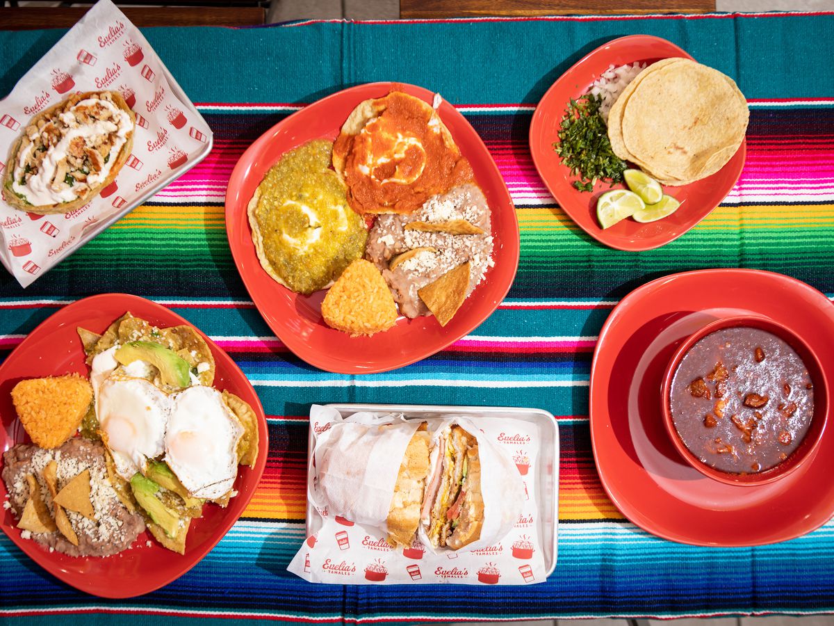An overhead photograph of a colorful table with chilaquiles, tortas, pancita, and other Mexican dishes.