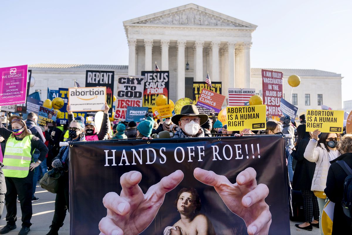 A banner in front of a group of protesters reads “Hands off Roe!” The United States Supreme Court building is behind the protesters.