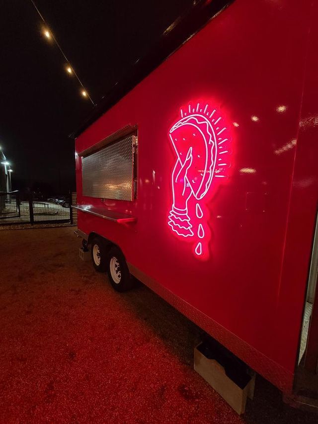 A red food truck with a pink neon sign that shows a hand holding up a taco.