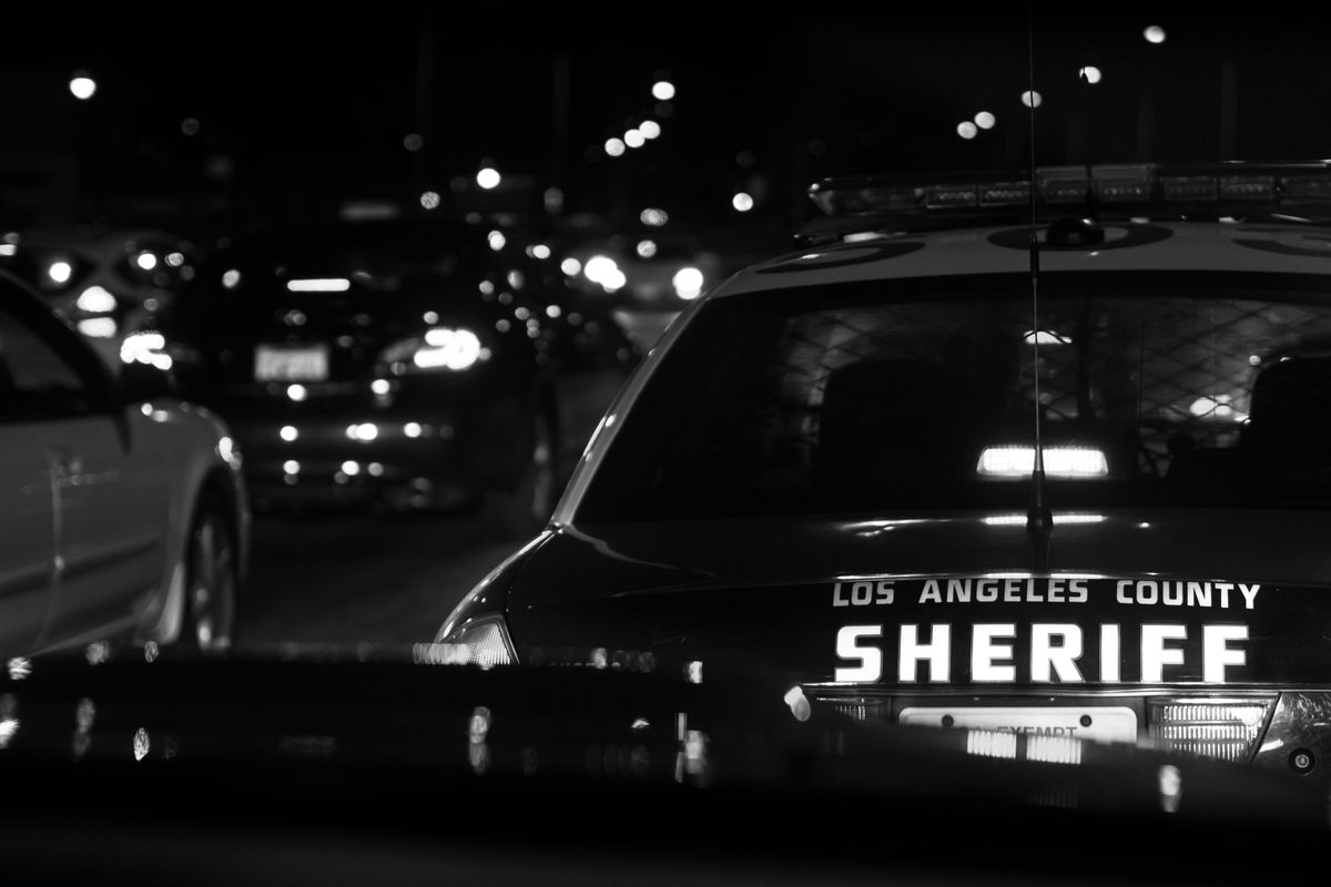 A squad car with the words “Los Angeles County Sheriff” on the back driving through traffic.