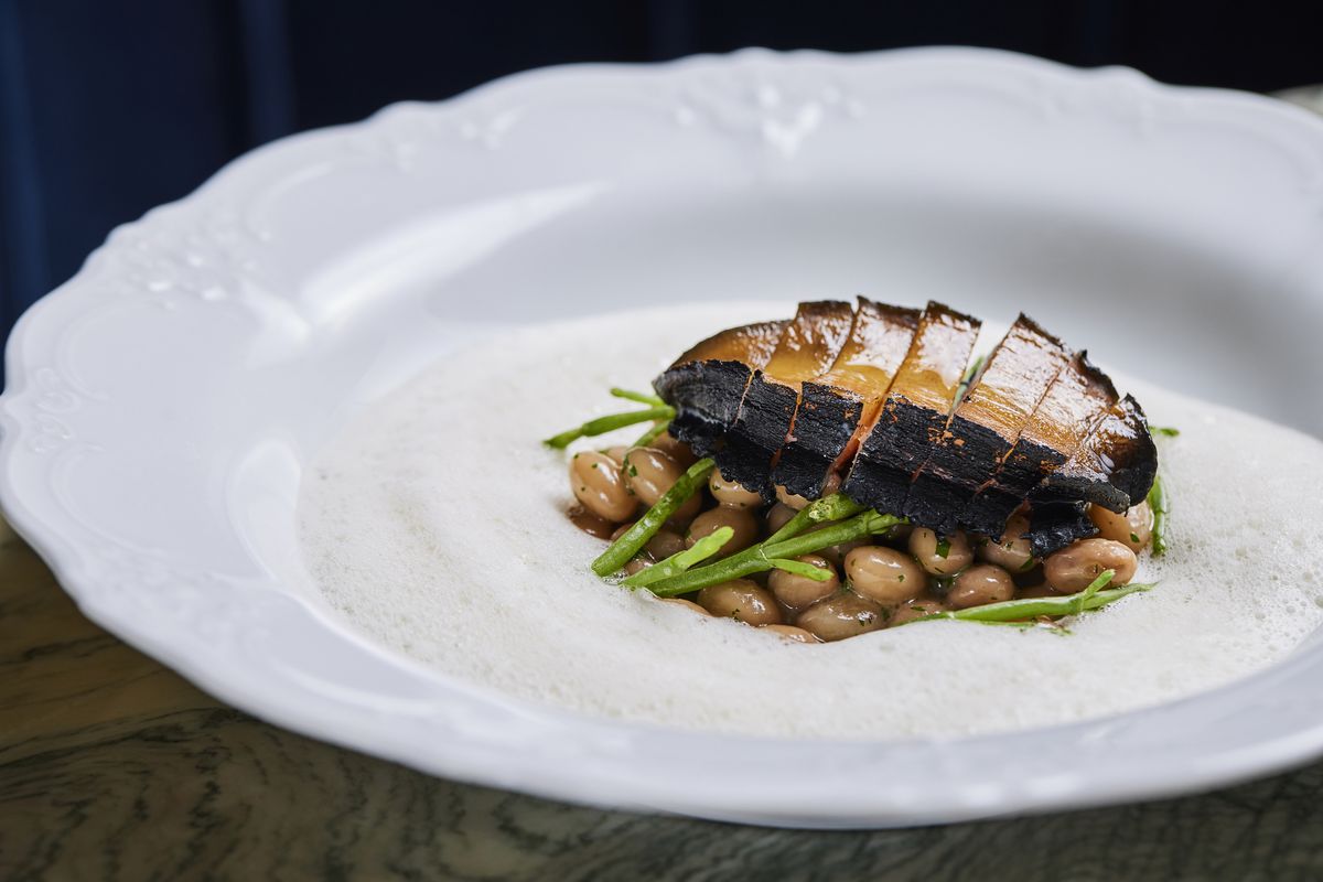 Plate of grilled sliced abalone with beans and a foam sauce in a white plate.