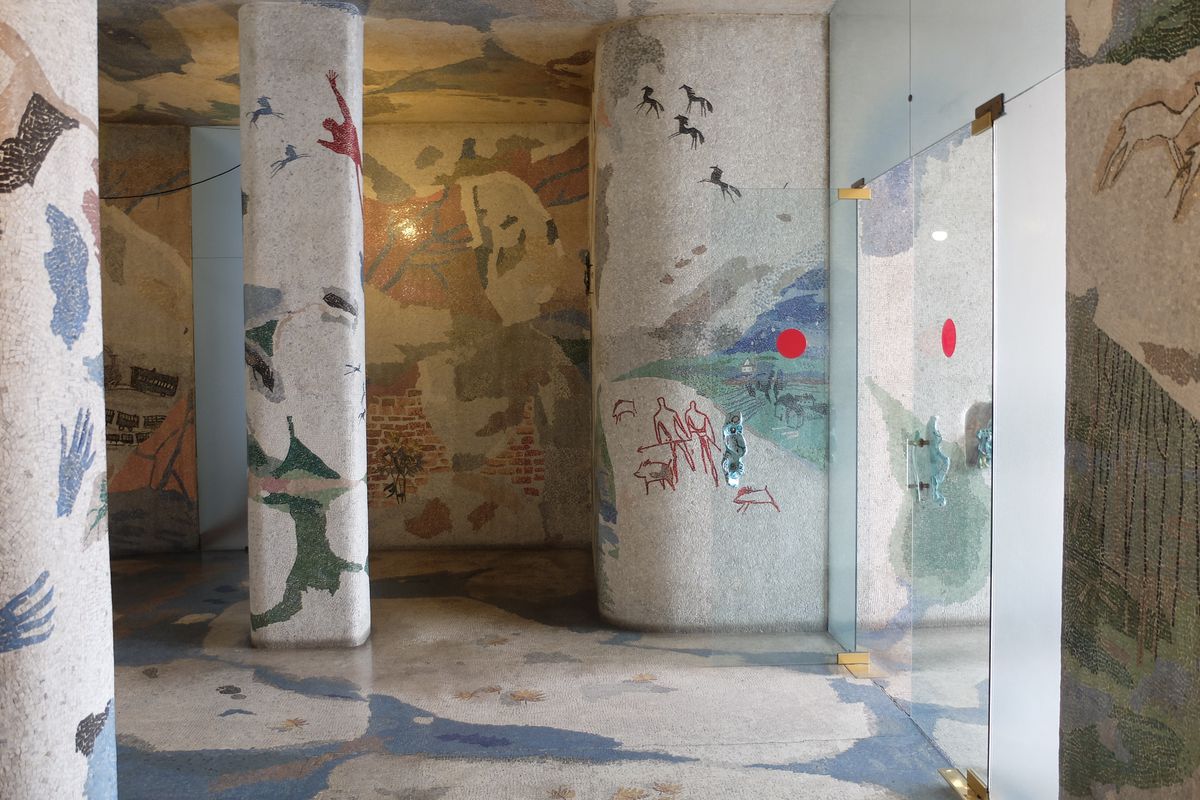 Photo of a lobby foyer with walls, columns, floors, and ceilings mosaiced with abstract shapes and hand prints and animals. 