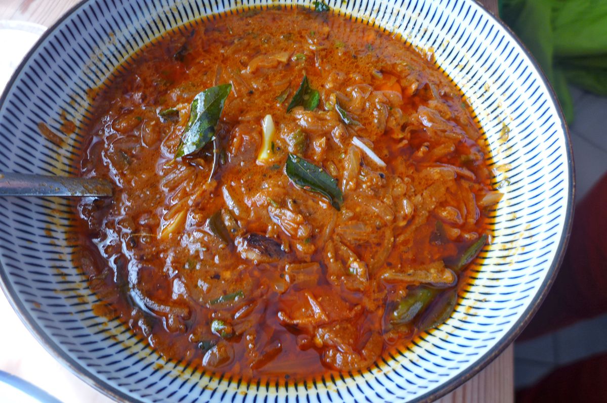 A blue bowl of red sauce with green leaves bobbing in it.