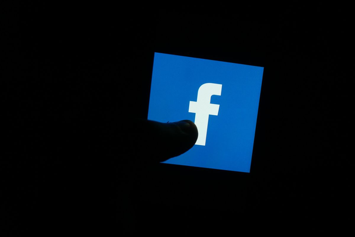 In this photo illustration a Facebook logo is seen displayed on a phone screen with a silhouetted thumb in front of it.