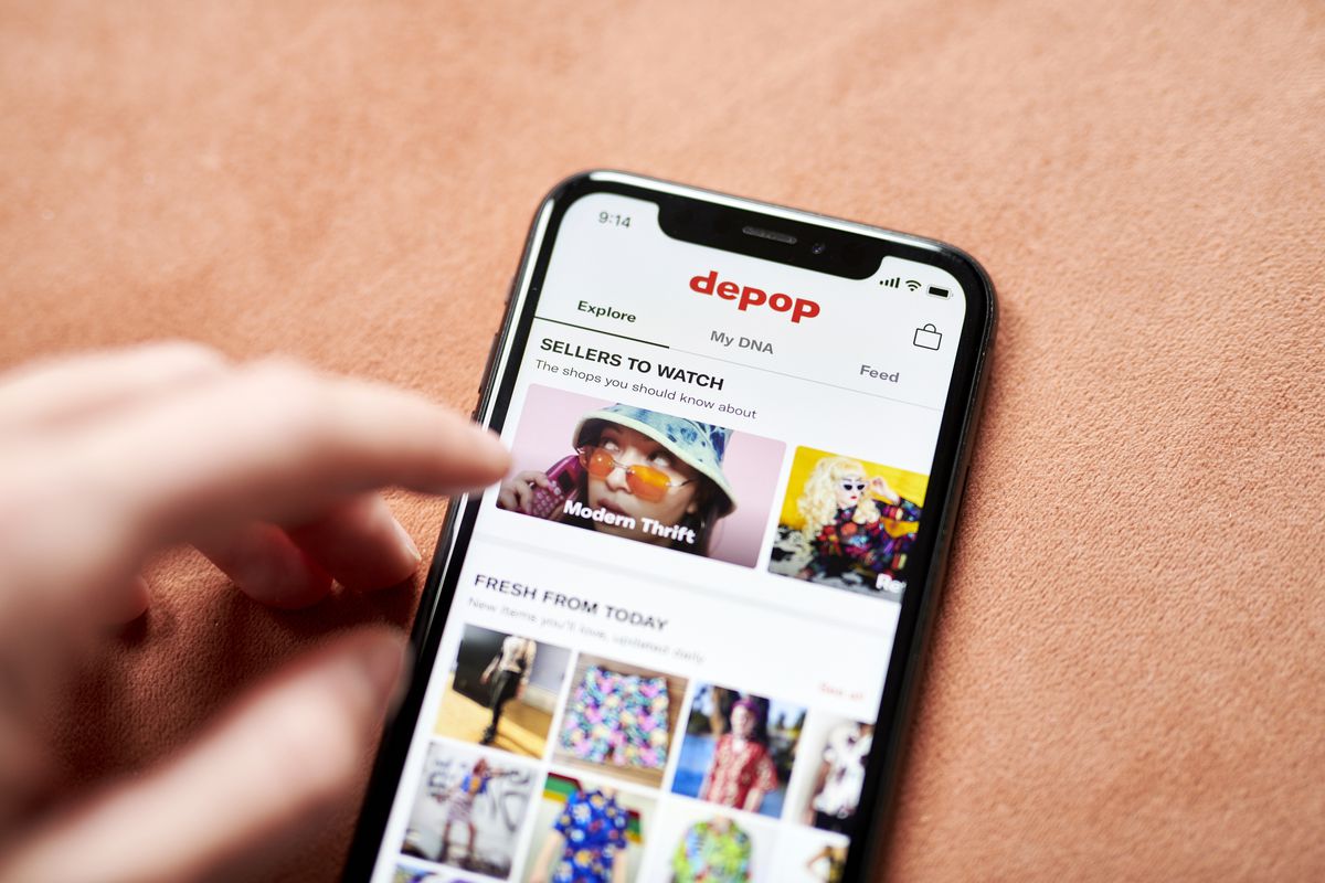 A hand hovering over a smartphone screen displaying the app Depop.
