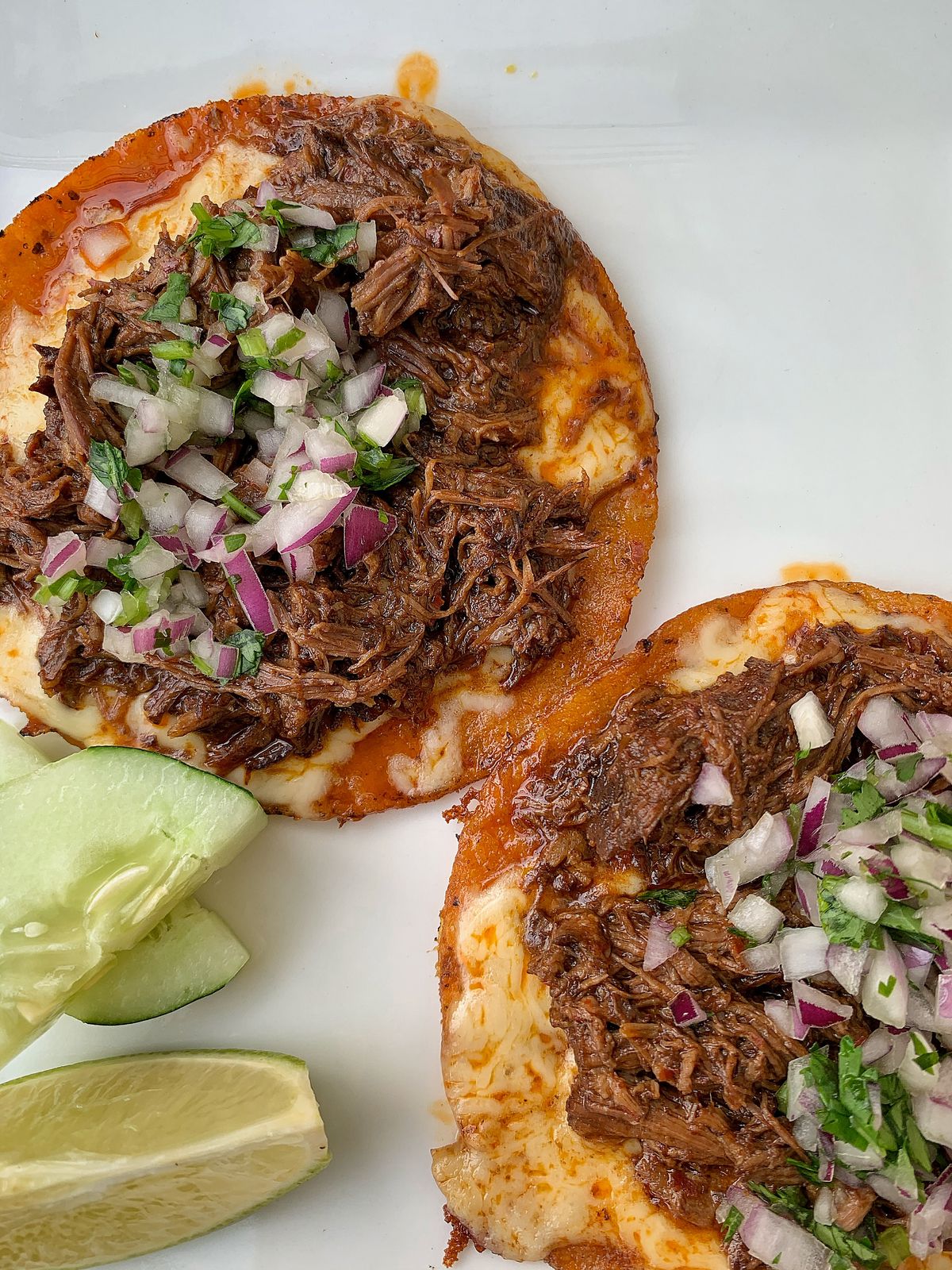Closeup of two meaty birria tacos, garnished with red onion, cilantro, and lime