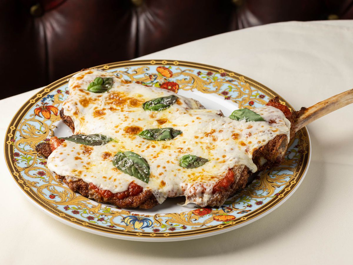 A colorful plate with a thinly pounded veal chop covered in sauce and cheese and basil.