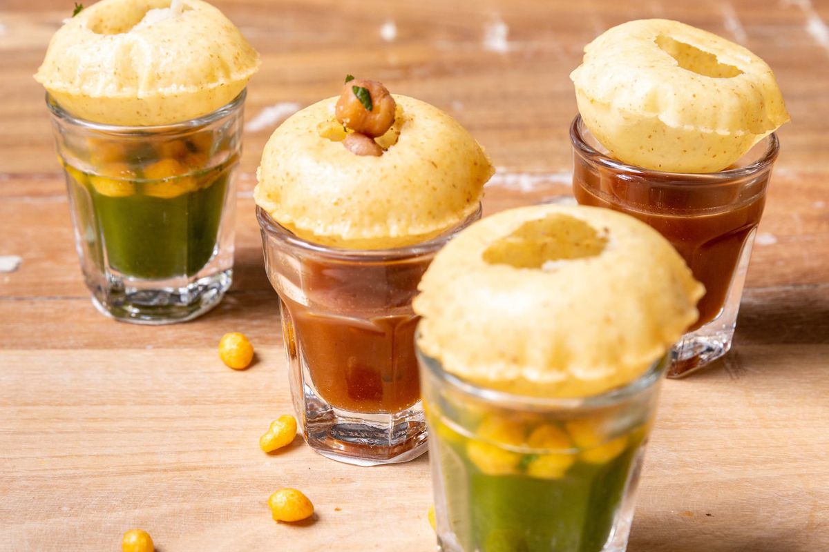 four glasses filled with tamarind and mint flavoured water, with a puri sitting on top of each one