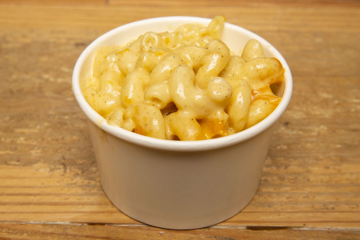 A white paper cup holds a serving of macaroni and cheese.