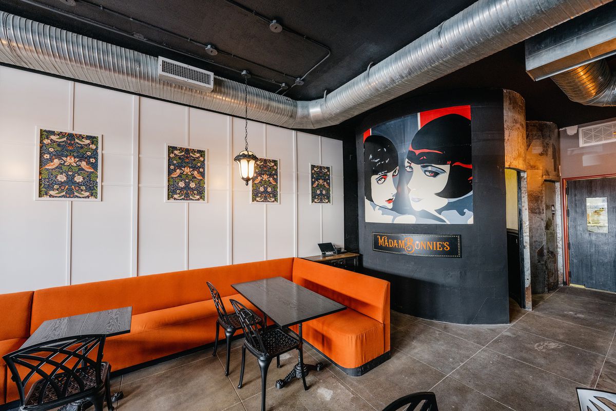 A lounge with orange booths and a poster of two women on the wall.