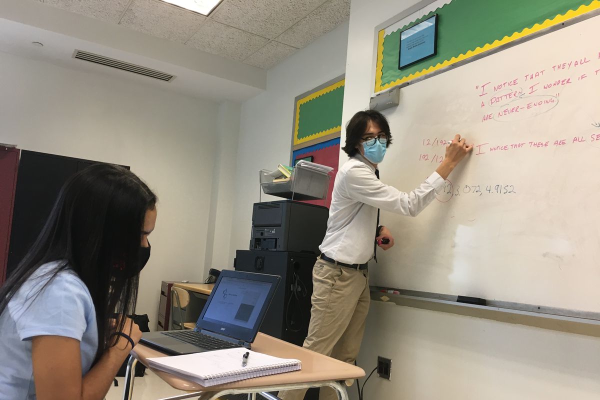 Ashanty Peralta sitting at her desk while Math teacher Austin Ha writes on a whiteboard.