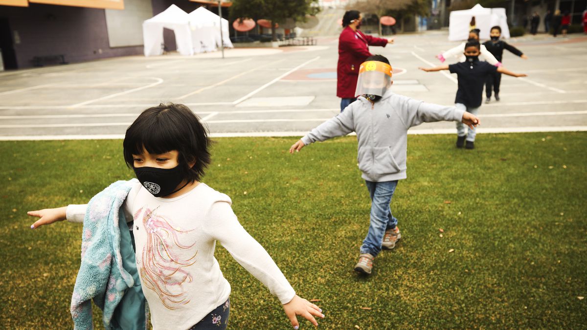 Children wearing face masks walk in a distanced line across a school’s grounds.