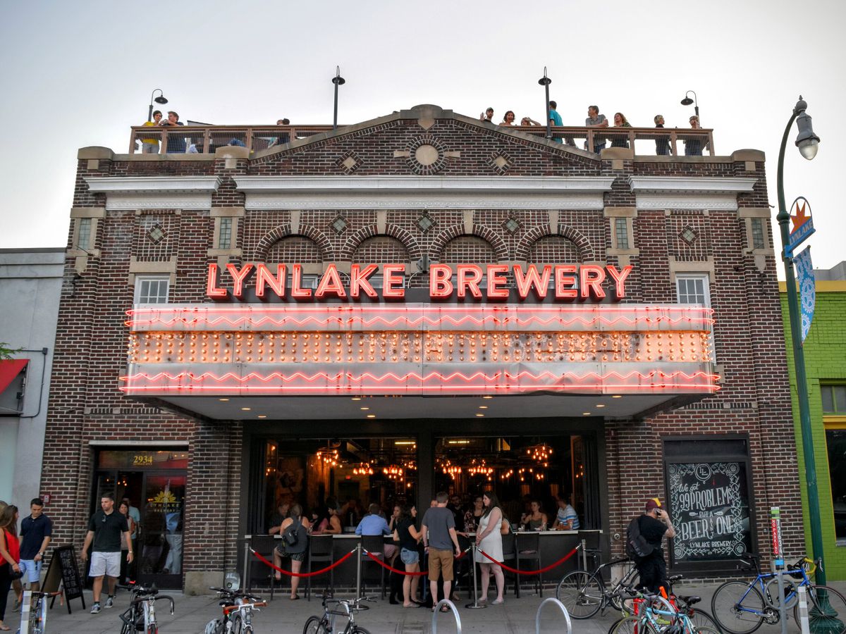 A large brewery exterior with a glowing orange sign that says “Lynlake Brewery” and people standing beneath it. 