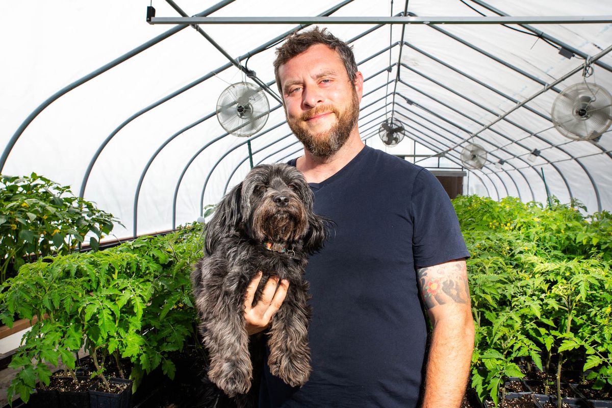 A man holds a dog in a greenhouse