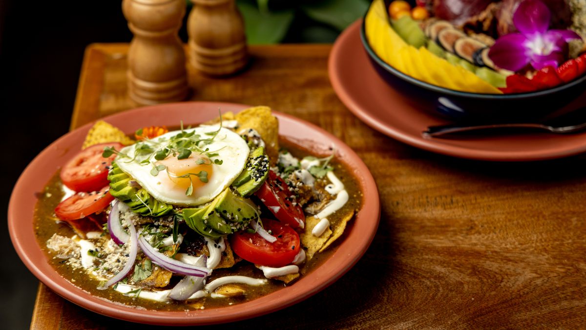 Ojo de Agua’s chilaquiles topped with a fried egg, cilantro, onions, and verde salsa, with an acai bowl  topped with fresh fruit on the side.
