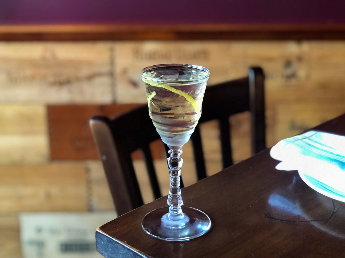 A clear martini sits in an elegant small glass with a citrus peel.