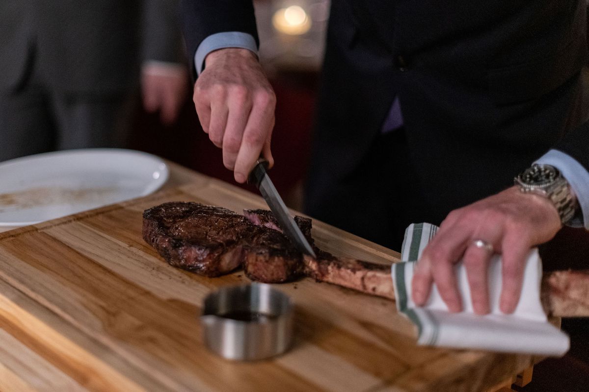 A server uses a long knife to cut a steak tableside.
