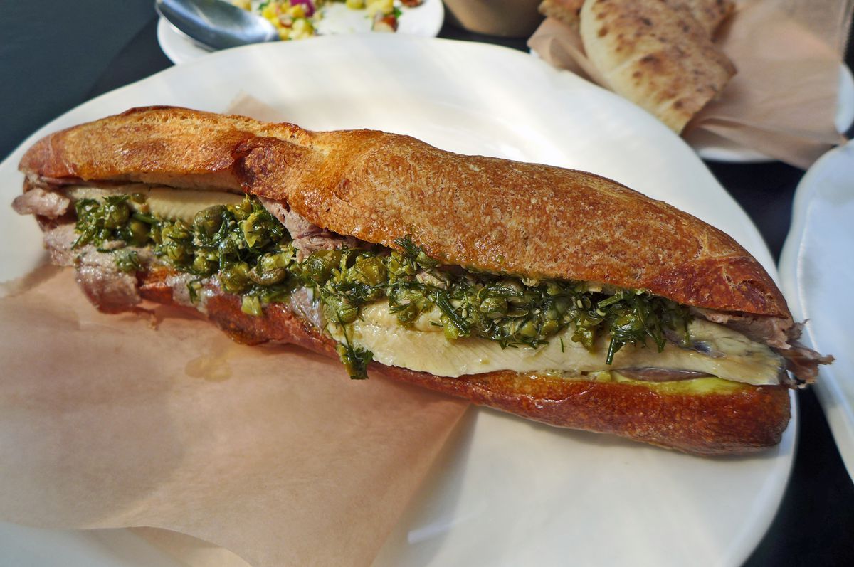 A long baguette with slices of tongue and green relish visible.