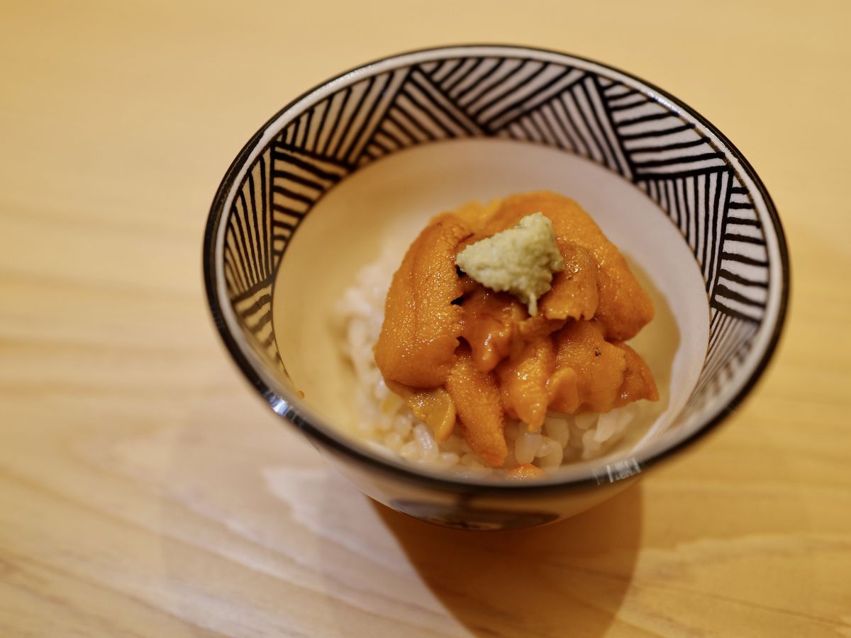 A ceramic bowl of rice topped with lobes of orange uni and a dab of wasabi.