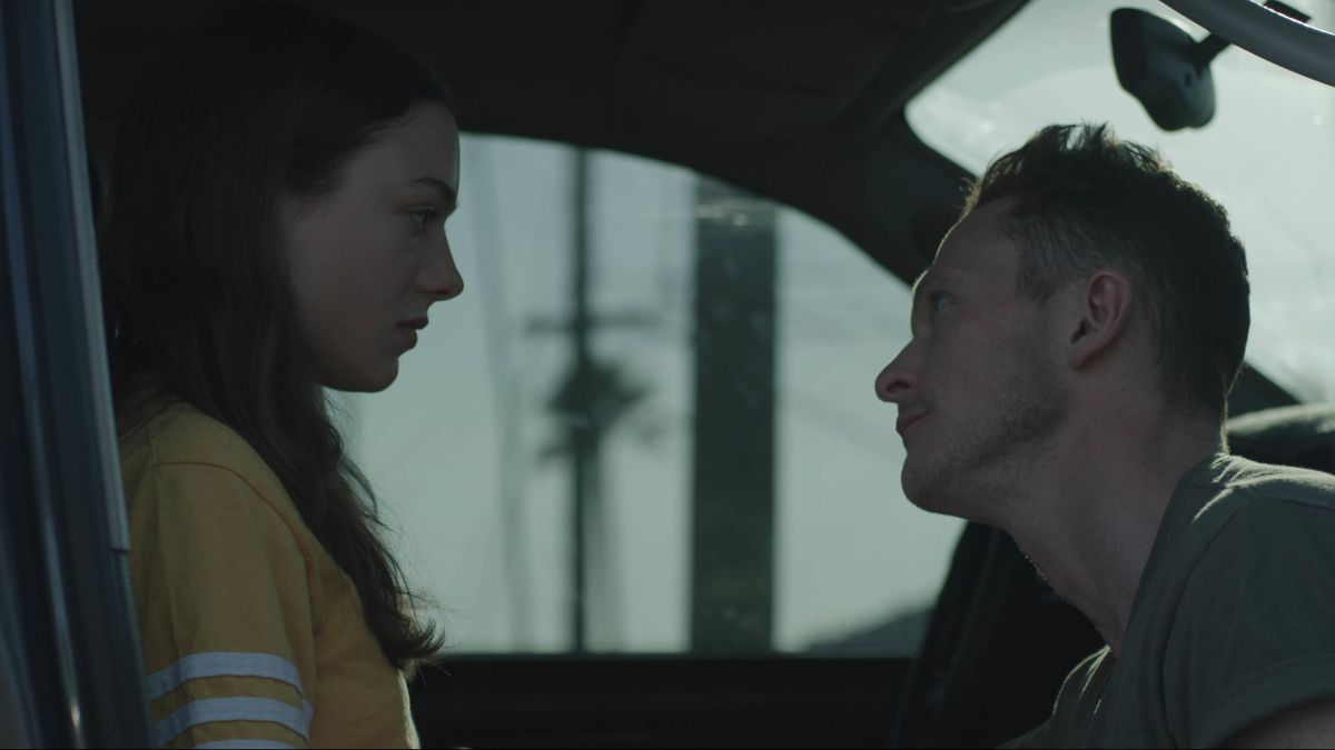 A teenage girl and an older man look at one another. They’re in the cab of a pickup truck.