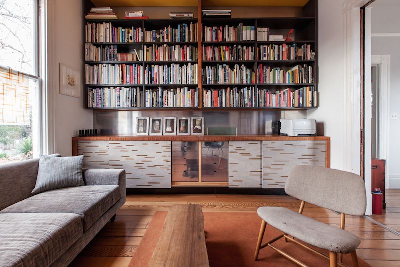 A room with a couch, chair, desk, and bookshelves with many books. 