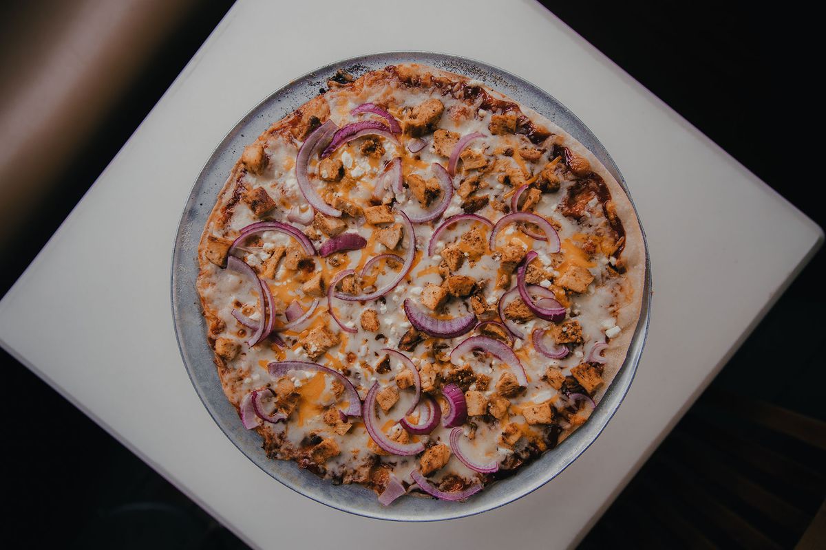 a barbecue chicken pizza topped with red onions, cheddar cheese, feta, and barbecue sauce
