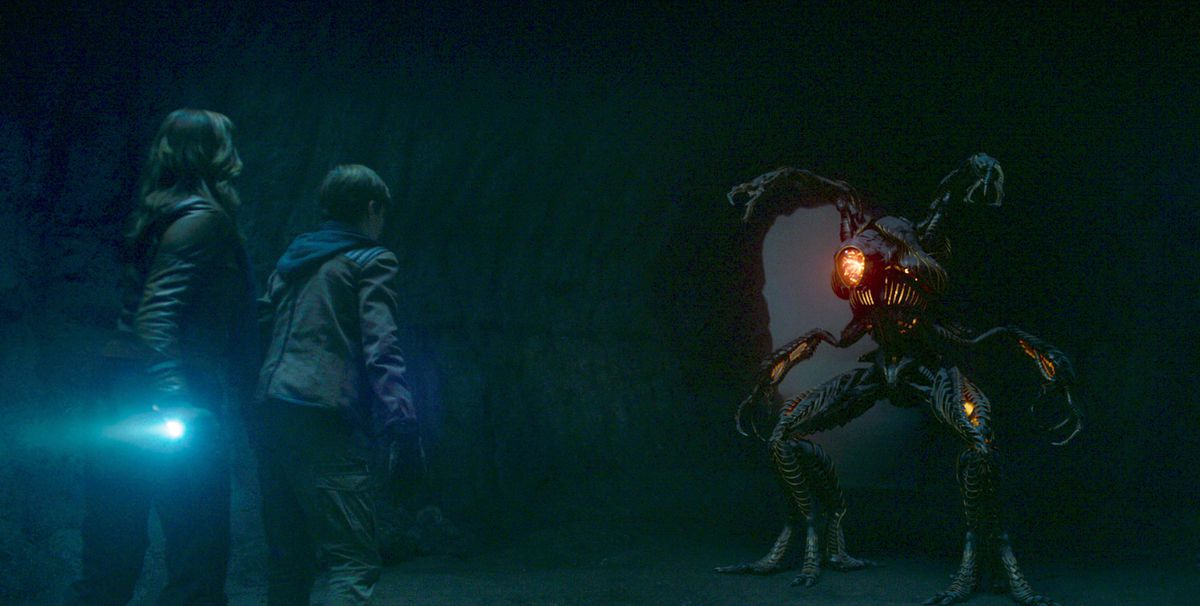 Two of the children of Lost in Space confronting an alien in a cave in a still from the show