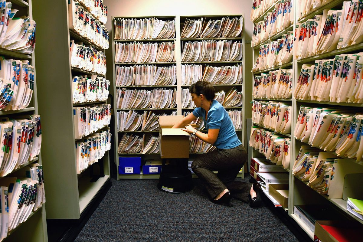 Woman kneeling in a room filled with medical files.