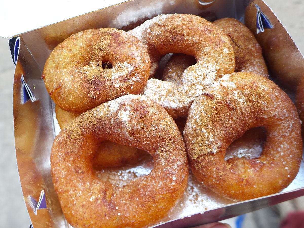 Four sugar-dusted loukoumades sit in a to-go box