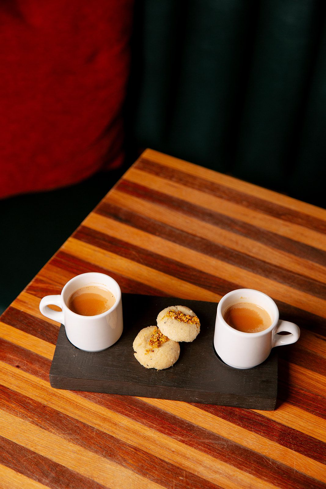 Two small cups of chai on a black plate with two shortbread cookies in the middle
