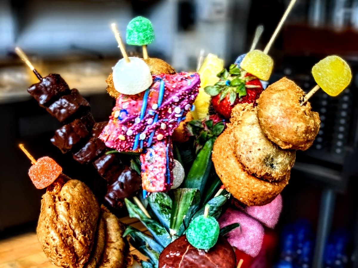 A pitcher of mimosas with skewers sticking out for garnish. The skewers include fried Oreos, creme pies, and gumdrops, among other colorful treats