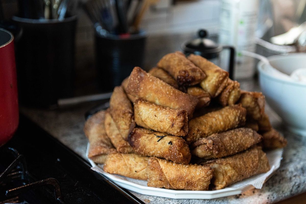 A pile of golden-brown fried egg rolls are stacked on a plate